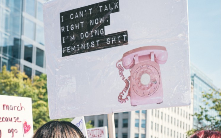 placard reading "I can't talk right now. I'm doing feminist shit." [Image by Gayatri Malhotra on Unsplash] 