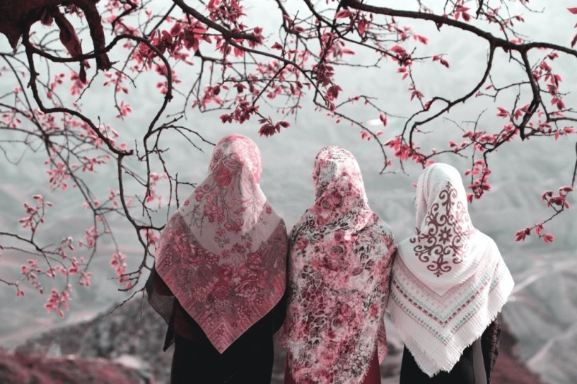 Three Muslim women facing away from the camera looking at blossoms